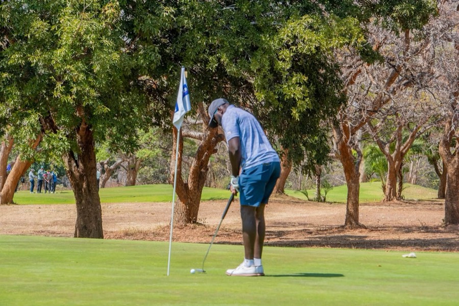 A golfer putts towards the flag under the trees